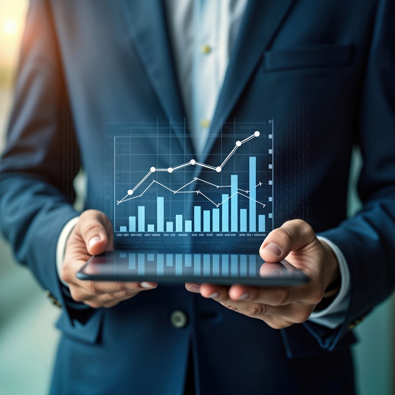Homme d'affaires en costume tenant une tablette. Un graphique de croissance numérique superposé affiche barres et lignes de tendance haussière. Analyse données performance marché.